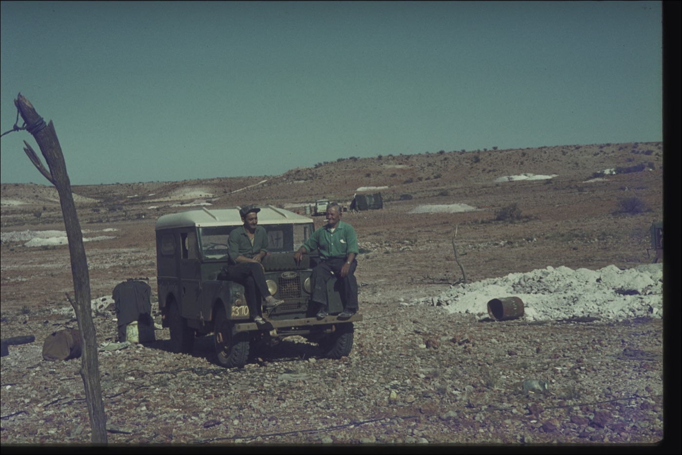Two old miners sharing a smoke on the bonnet of George Sr's Land Rover, Eight Mile field, circa 1959