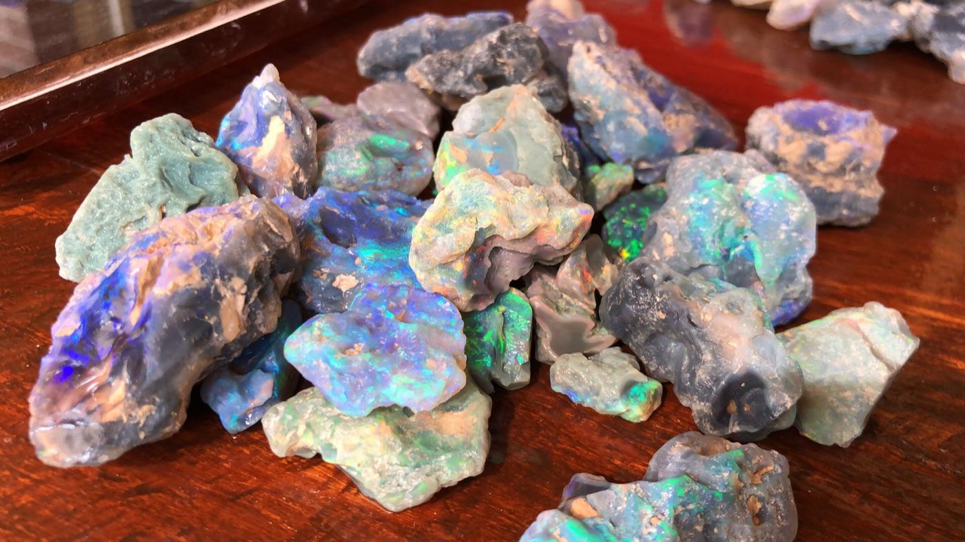 Rough Lightning Ridge black opal on a wooden table, showing blue and green colour through the potch