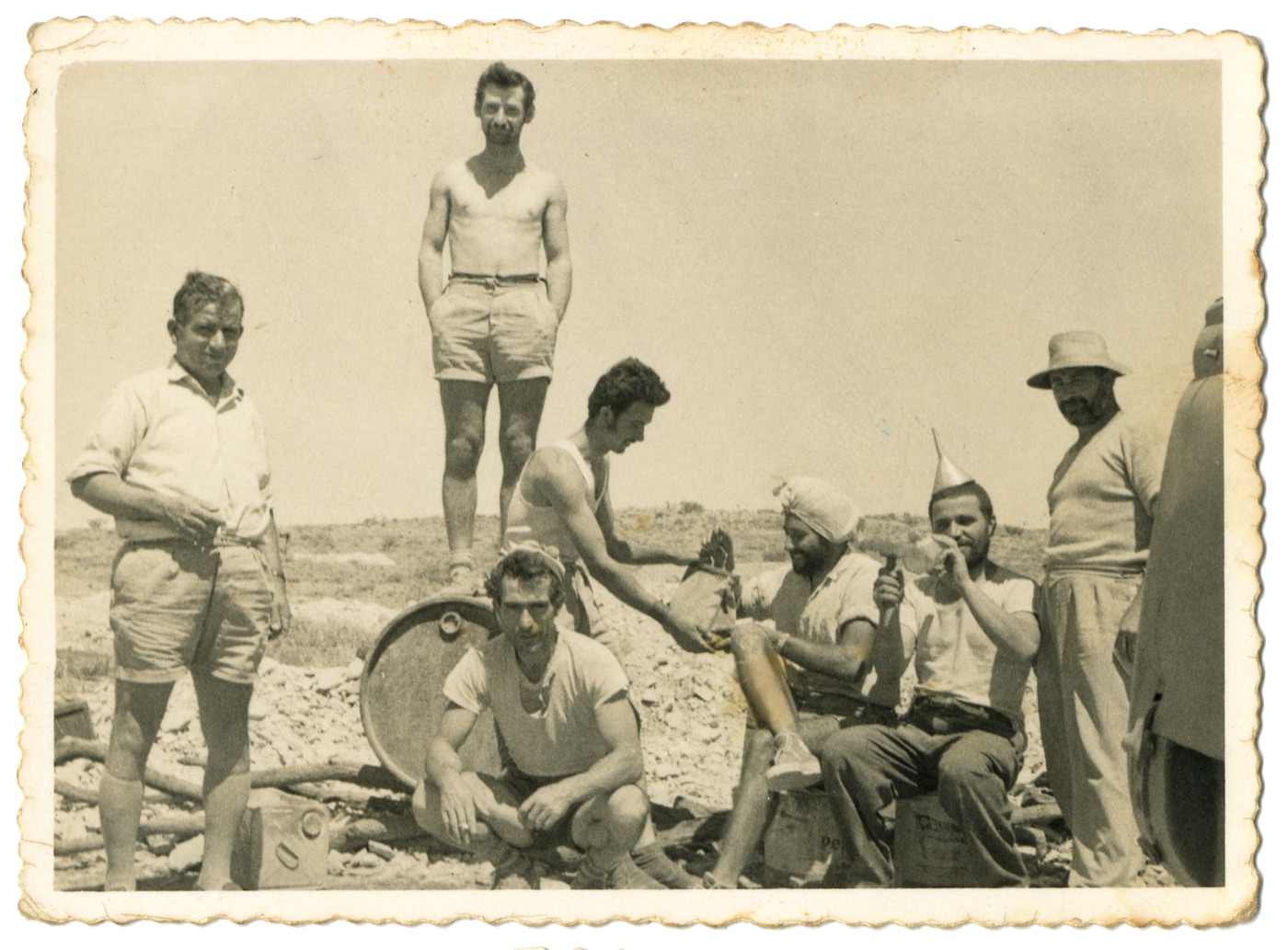 George Sr and the mining team at lunch on the Eight Mile field, one man playfully wearing an oil funnel as a hat, 1960